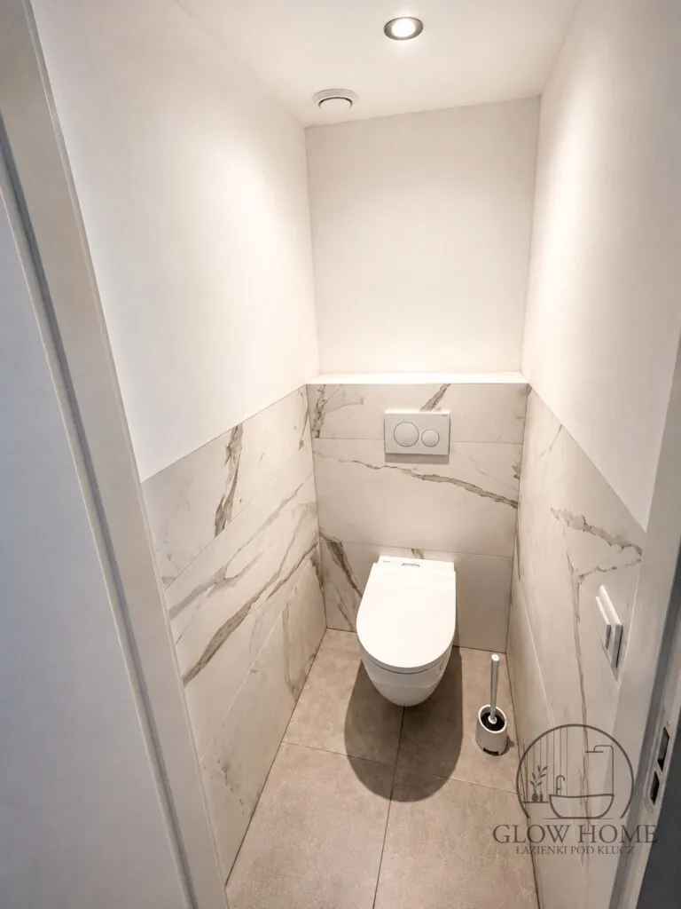 Wąska łazienka z jasnymi płytkami i WC podwieszanym na stelażu