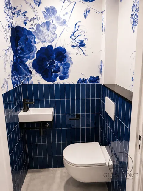 Granatowe kafle metro i tapeta w niebieskie kwiaty, biała umywalka i WC